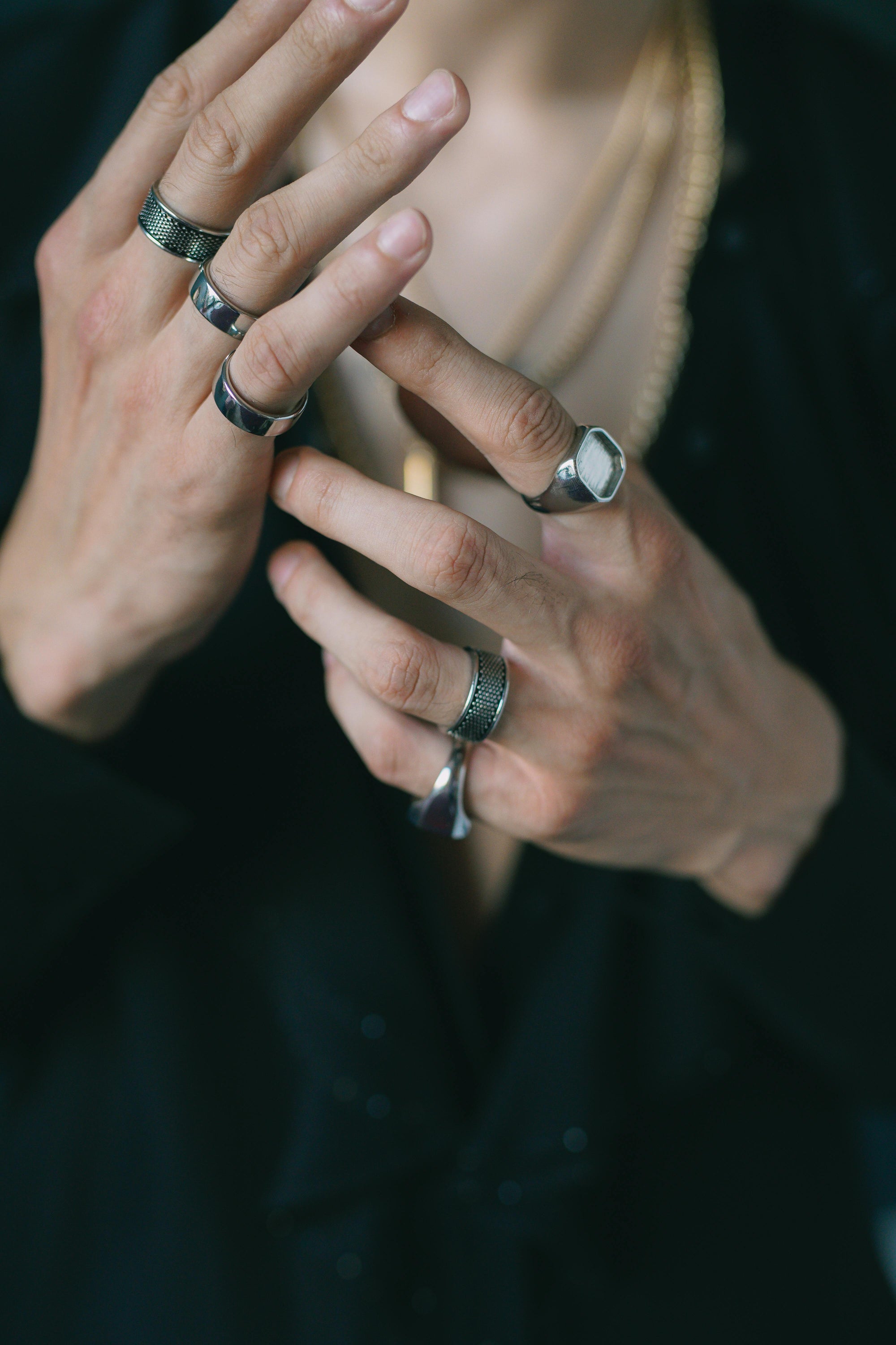 Close-up of hands with multiple rings on fingers against a dark background